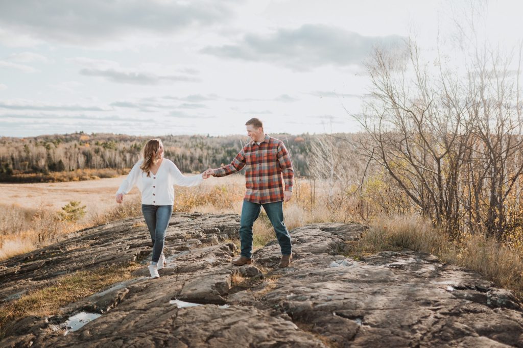 Couple holding hands walking on rocky overlook. 
